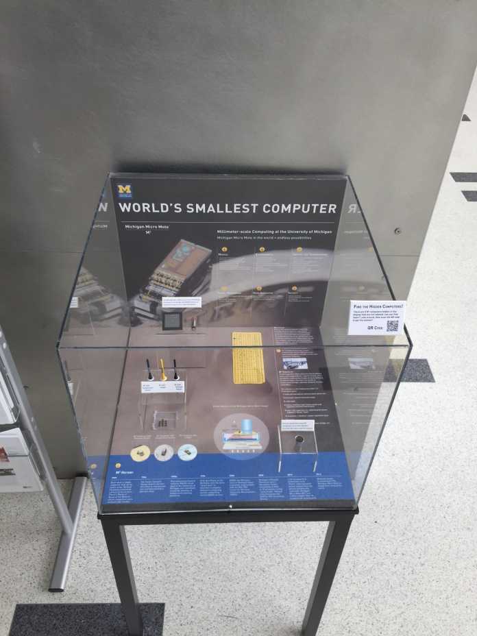 Der winzige Computer &quot;Michigan Micro Mote&quot; in einem Glaskasten des Computermuseums. Die gelbe Lochkarte im Hintergrund enthält einen M3 - er passt in eines der ausgestanzten Löcher.