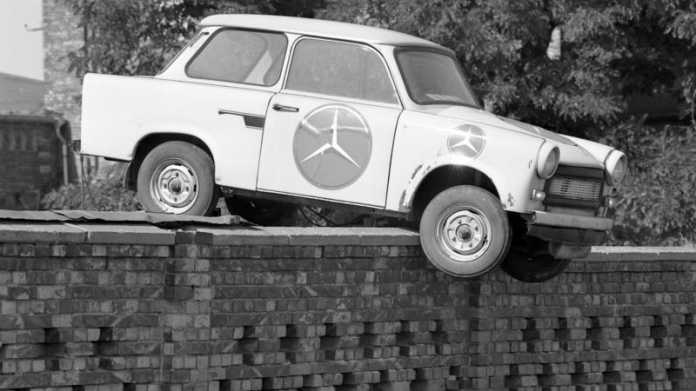 Trabi mit großem Mercedes-Stern.Aufkleber hängt über Mauer