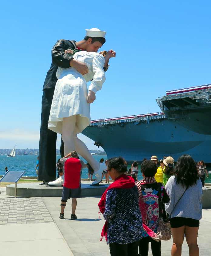 Touristen, dahinter eine riesige Statue: Matrose küsst Mädchen