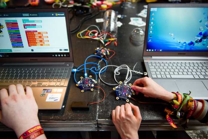 Zwei aufgeklappte Laptops, dazwischen spielen Kinderhände mit zwei sternförmigen Mikrocontrollern, den Calliope Minis