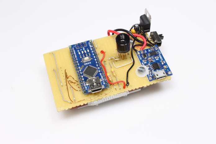 Gelbe Lochrasterplatine von vorn mit einem blauen Arduino Nano, schwarzen Infrarotsensor und blauem LiPo-Lademodul sowie weiteren elektrischen Bauteilen
