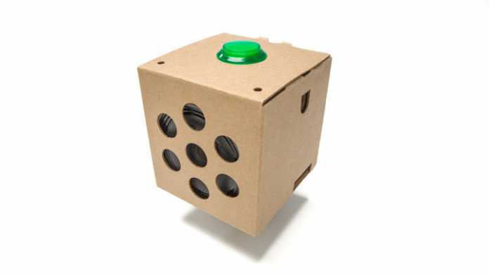 Ein brauner Pappwürfel mit grünem Button oben und Lautsprecher hinter großen Löchern an der Seite