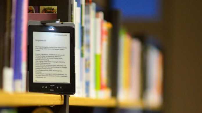 Ein E-Book-Reader steht in Mitten von Büchern im Regal.