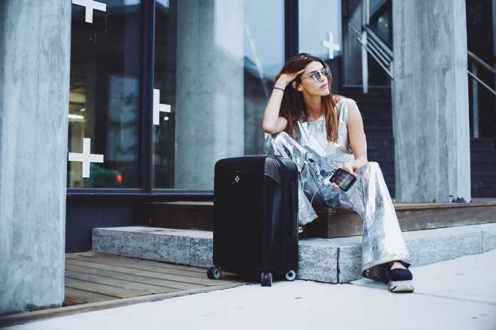 Frau sitzt neben Koffer vor einem Gebäude