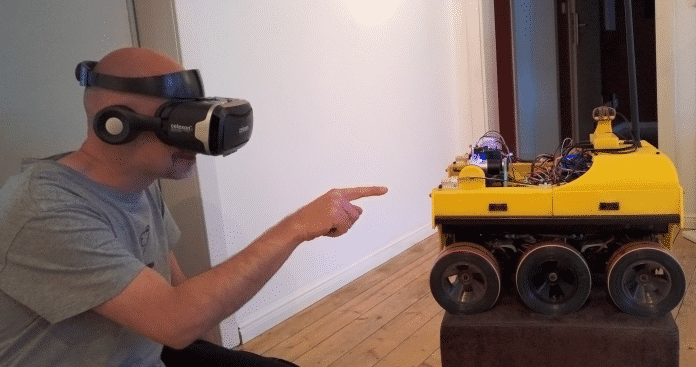 Ein Mann mit VR-Brille zeigt auf einen gelb-schwarzen Roboter