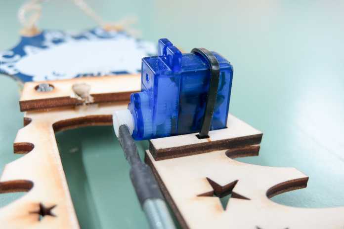 Blauer Servo, der mit Kabelbinder auf dem Holz befestigt ist.