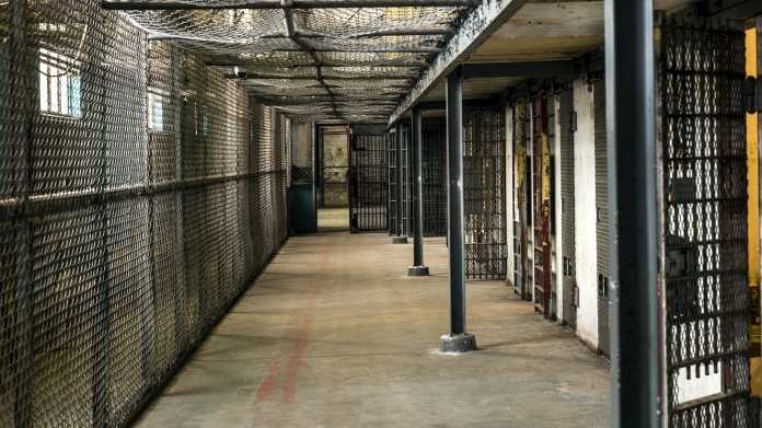 Vergitterter Gang in einem Gefängnis, rechts Zellentüren