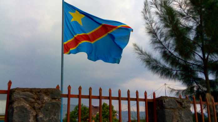 Fahne der DR Kongo weht auf einem Mast hinter einem Zaun