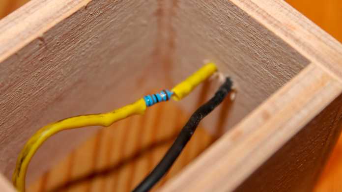 In einem Holzrahmen hängen zwei Kabel, in einem ist eine LED eingelötet. Außen ist Schrumpfschlauch.