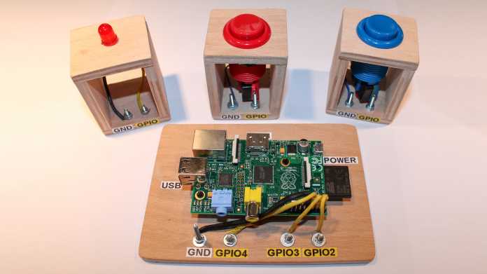 Holzbrett mit Raspberry Pi neben drei Holzwürfeln mit LED bzw. Taster.