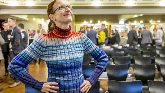 Eine Frau steht in einem Vortragsraum, ihr Pullover ist geringelt mit blauen und roten Streifen.