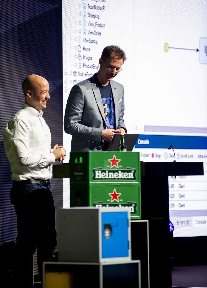 Johan den Haan zeigt zusammen mit einem seiner Mitarbeiter eine native Anwendung unter Mendix Mobile. Die Anwendung öffnet via TouchID einen Tresor, in dem sich ein Bier befindet.