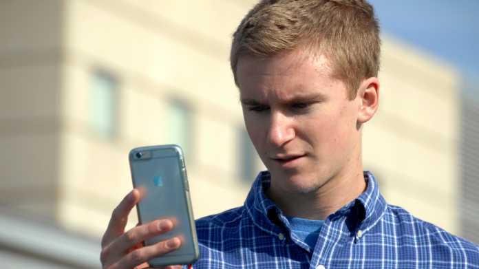 Junger Mann blickt stirnrunzelnd auf sein Handy