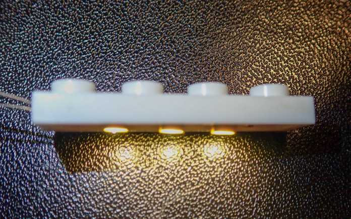 Ein weißer Lego-Streifen mit vier Noppen, auf der Unterseite sind drei LEDs befestigt.