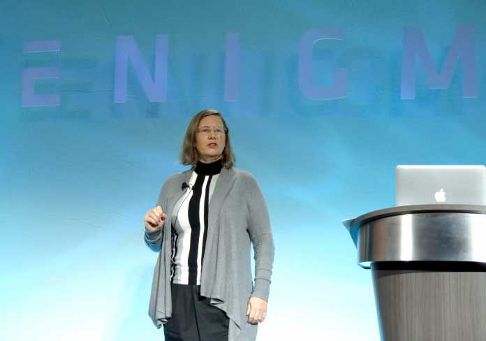 Weiße Frau auf Bühne neben Rednerpult, dahinter blaue Wand mit Schriftzug ENIGMA