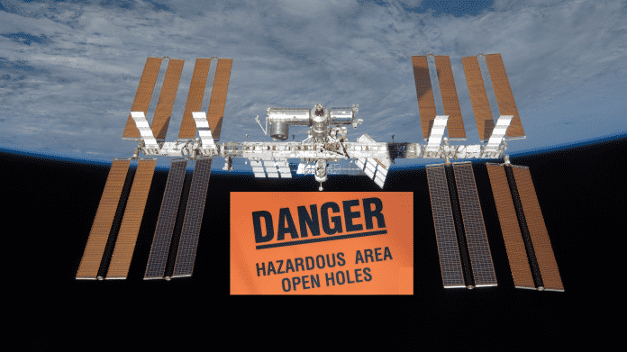 ISS über der Erdkugel, davon ein Riesenschild "Danger - Hazardour Area Open Holes"