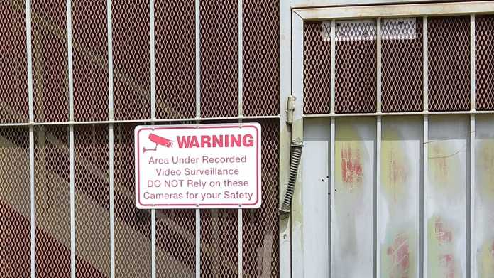 Gittertor mit Warnung vor Videoüberwachung, auf die man sich nicht verlassen möge