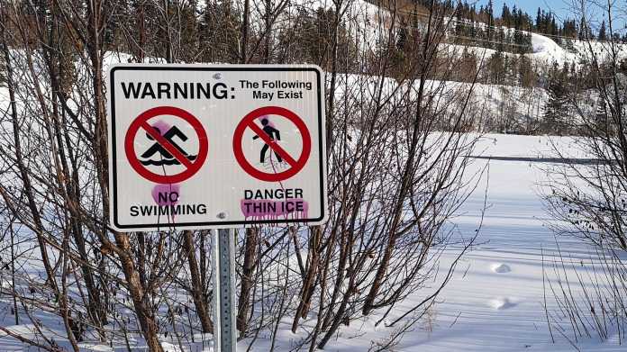 Warnschild vor verschneitem See verbietet Schwimmen und warnt vor dünnem Eis