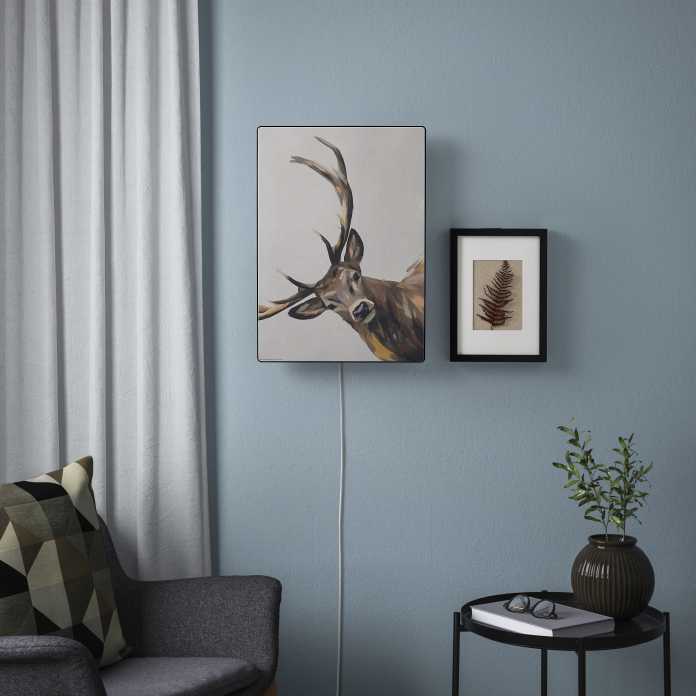 Symfonisk-Lautsprecher mit Hirsch-Gemälde darauf hängt neben einem anderen Bild an einer hellblauen Wand