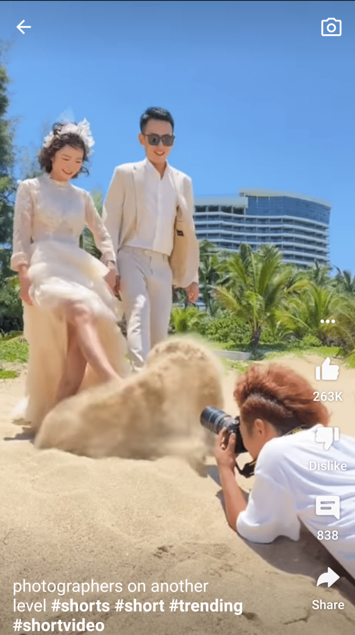Hochzeitspaar kickt Sand auf eine Fotografin