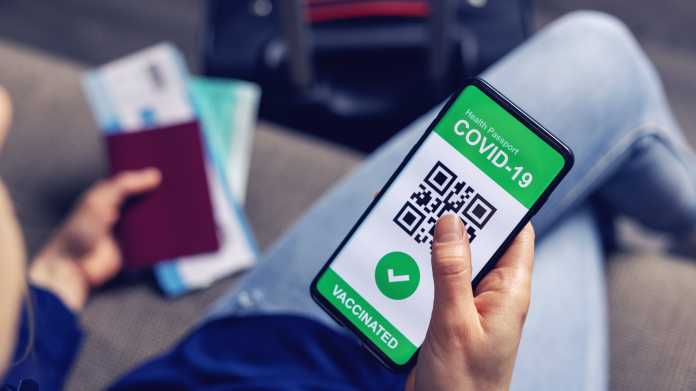 Person mit Reisepass und digitalem Impfnachweis in einer Smartphone-App wartet auf dem Flughafen. 
