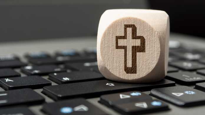 Ein auf einer Computertastatur liegender weißer Würfel zeigt ein Kreuz