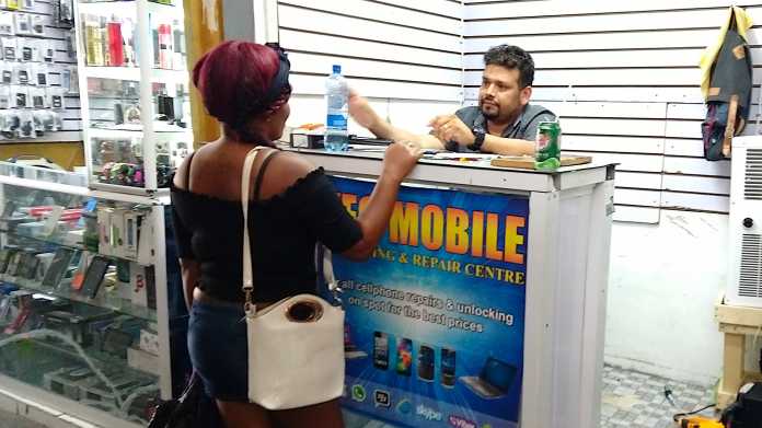 Kleiner Laden für Handy-Reparatur in einer Markthalle. Ein Mann hinter dem Tresen bedient gerade eine Kundin.