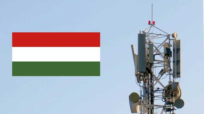 Rechts ein Mobilfunk-Sendemast mit mehreren Antennen, links schwebt die ungarische Flagge