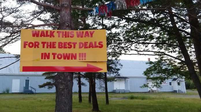 Schild an Baum: "Walk this way for the best deals in Town!!!"