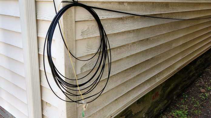 Mehrere Schleifen schwarzen Coaxial-Kabels hängen an der Außenwand eines Gebäudes, quer darüber hängt ein gelbes Ethernet-Kabel