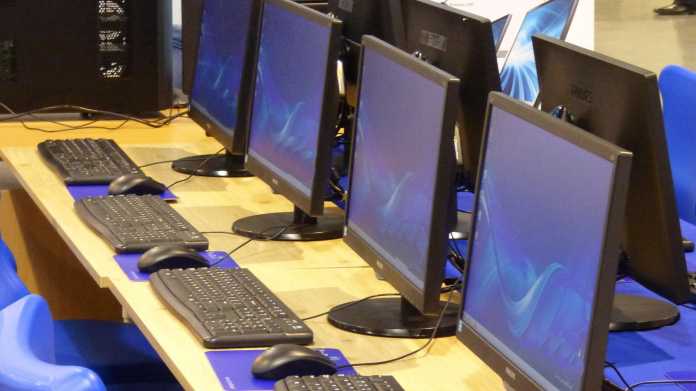 4 Computermonitore samt Tastaturen und Mäusen stehen in einer Reihe auf Tischen