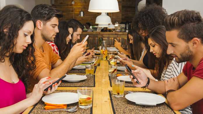 Junge Menschen starren am Esstisch auf ihre Handys