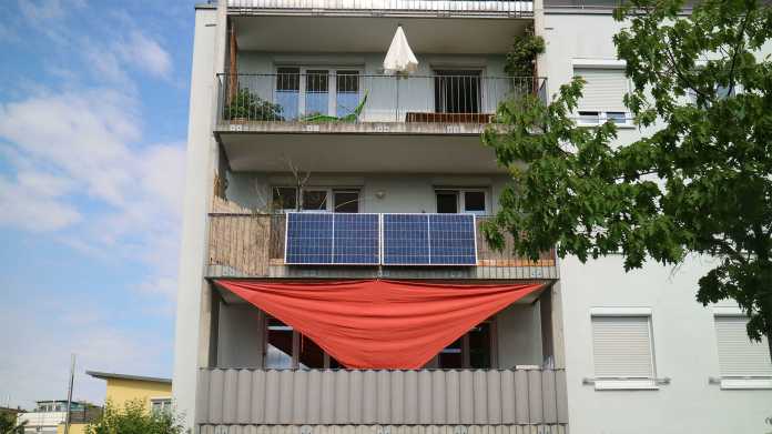 Foto einer Gebäudefassade mit Balkonen. An einem Balkongeländer hängen Solarmodule.