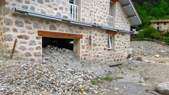 Steinernes Haus mit gebrochenen Fenstern; aus der Garage quillt ein Haufen aus Steinen und Felsbrocken