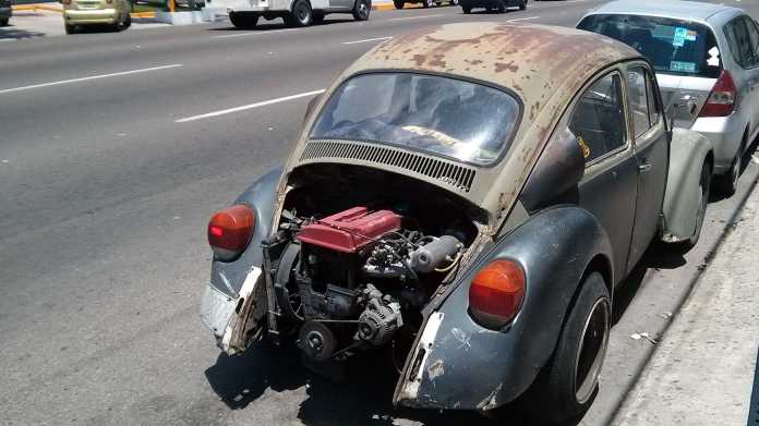Ein alter, rostiger VW Käfer dessen Motorhaube (hinten) fehlt, weil ein zu großer Motor eingebaut wurde