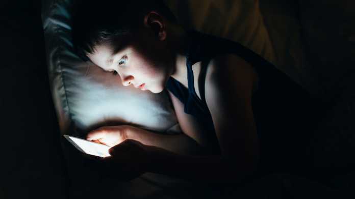 Kind schaut im Dunkeln auf ein beleuchtetes Display