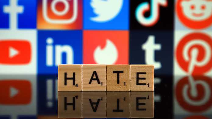 Würfel zeigen die Buchstaben HATE, darhinter Logos sozialer Netzwerke