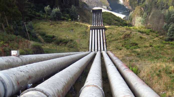 Sechs große Wasserrohre führen einen Abhang hinab hin zu einem Turbinenhaus
