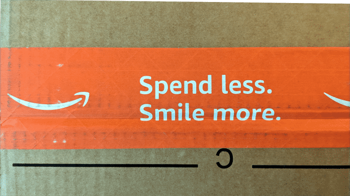 Detailaufnahme eines Amazon-Pakets. Auf dem orangen Klebeneband steht neben dem Amazon-Logo "Spend less. Smile more."