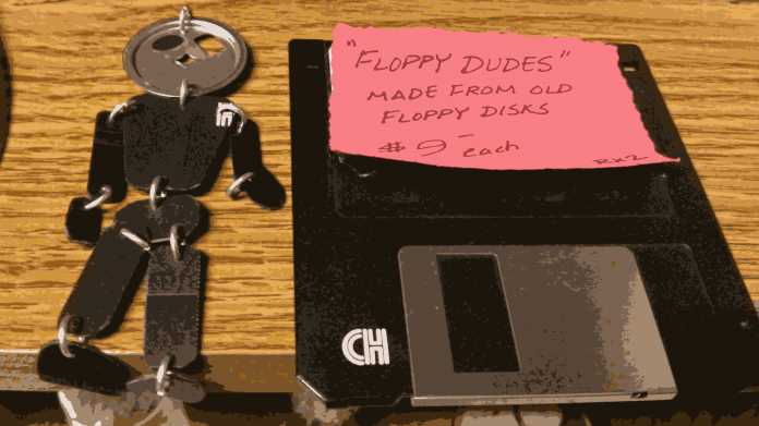 Rechts eine 3,5-Zoll-Diskette, links ein von Künstlerhand aus Diskettenteilen gefertigtes Männlein; ein Notizzettel auf der Diskette sagt "'Floppy Dudes' made from old floppy disks, $9 each"