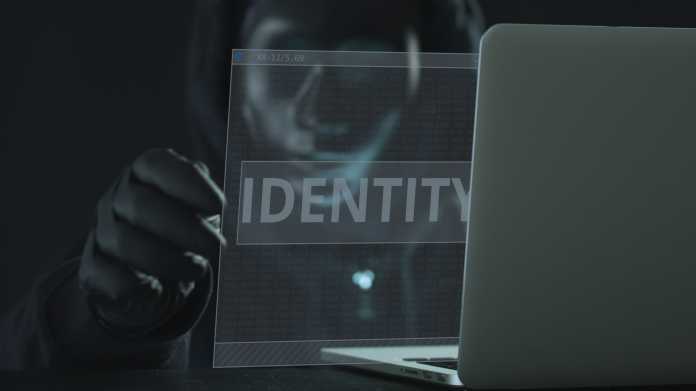 Künstlerische Darstelölung "Cyberkriminalität: Eine verhüllte, maskierte Person zieht eine transparente Folie mit Aufschrift "Identity" aus einem Laptop