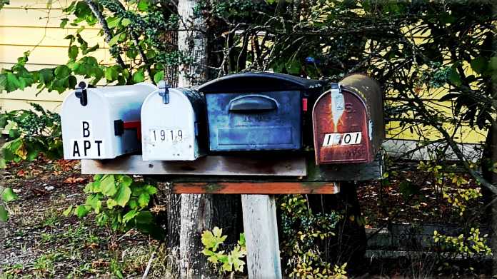 Vier unterschiediche Hausbriefkästen auf einer schiefen Holzstange warten auf Post