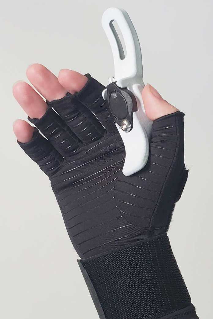 Eine Hand trägt einen Handschugh, dessen Fingerkuppen fehlen; zwischen Daumen und Zeigefinger hält sie ein kleines, aufgkelapptes Gerät