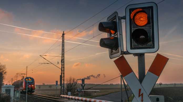 Rote Ampel an Bahnübergang mit geschlossenem Balken und nahendem Personenzug