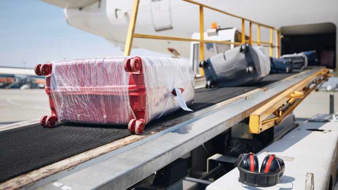 Koffer werden über ein Transportband in den Gepäckraum eines Passagierflugzeugs befördert.