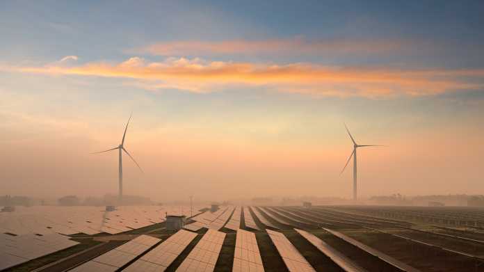Windkraftanlagen hinter Solarpaneelen in der Landschaft