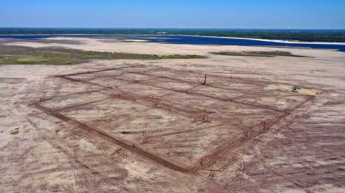 Luftaufnahme: trockenes Erdreich, im Hintergrund Wasser; im Erdreich stecken Stahlrohre