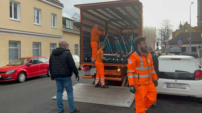 5 Personen, davon 3 in orangen Uniformen, verladen E-Scooter in einen LKW