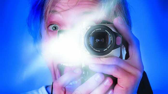 Auf dem Bild ist ein Kopf von einem Mann auf blauem Hintergrund zu sehen, der sich selbst mit Blitzlicht fotografiert, ein Auge ist zu sehen, das andere schaut in die Linse. 