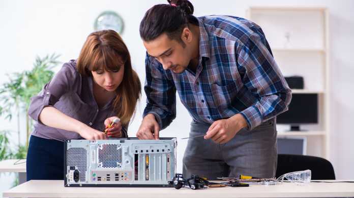 Zwei Menschen reparieren einen Computer und beugen sich mit Werkzeug in der Hand über ein geöffnetes PC-Gehäuse.